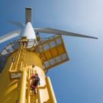 Engineers climbing wind turbine from boat at offshore windfarm, low angle view